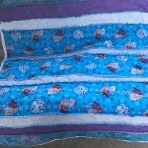 May include: A blue and purple patchwork quilt with a Frozen theme. The quilt features images of Elsa, Anna, and Olaf. The quilt is made with a variety of fabrics, including cotton and flannel.