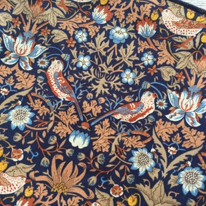 May include: Close-up of a fabric with a repeating pattern of birds, flowers, and foliage in shades of navy blue, orange, tan, and light blue. The design features stylized birds with red and white markings, surrounded by floral and leaf motifs.