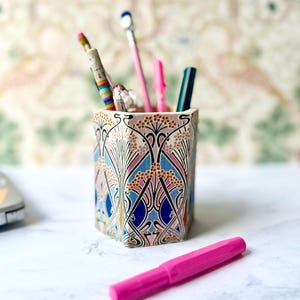 May include: A white ceramic mug with a black handle and the text "But First, Coffee" in a handwritten style. The mug is on a white surface. The mug is approximately 10 cm tall.
