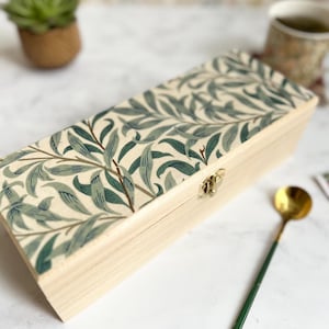 May include: A wooden box with a hinged lid and a gold latch. The box is covered in a green and white floral patterned paper.