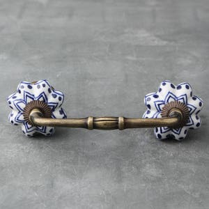 May include: A white ceramic drawer pull with a blue and white floral pattern. The pull has a brass bar connecting the two ceramic pieces.