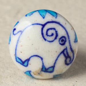 Puede incluir: Pomo de cerámica blanco con un diseño de elefante azul y blanco. El elefante tiene un remolino azul en la cabeza y detalles azules alrededor del cuerpo.