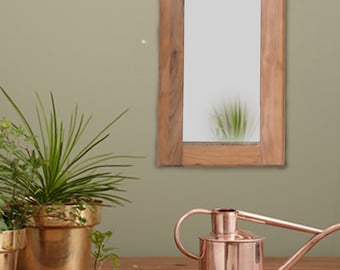 May include: A wooden framed mirror with a rectangular shape and a light brown finish. The mirror is hanging on a light green wall.