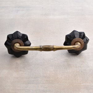 May include: Black ceramic drawer pull with a gold metal arm. The pull has a decorative design on the ceramic knobs.