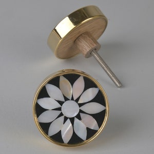 May include: A round, black and white, decorative cabinet knob with a gold rim. The knob features a white flower design made of mother of pearl.