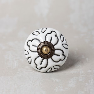 Pode incluir: Botão de cerâmica branco com um design floral preto e um acento de latão. O botão é redondo e tem uma superfície lisa.