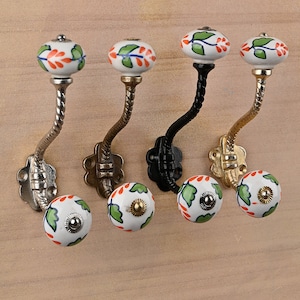 May include: Set of four decorative hooks with a twisted metal design and ceramic knobs. The knobs are white with green leaves and orange accents.