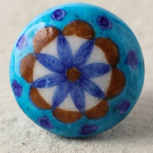 May include: A blue ceramic knob with a white and brown floral design. The knob has a blue and white flower in the center surrounded by a brown ring.