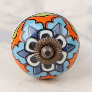 May include: A colorful ceramic knob with a blue, orange, and green floral design. The knob has a metal screw in the center.