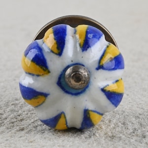 Könnte beinhalten: Ein weißer Keramik-Knopf mit einem blau-gelben Streifenmuster. Der Knopf hat eine Messingbasis.