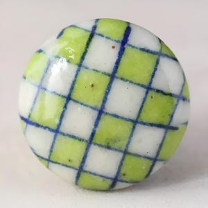 May include: A round ceramic knob with a green and white checkered pattern and blue lines.