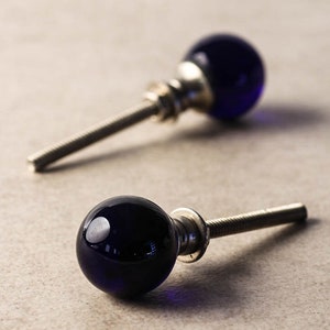 Może przedstawiać: Dwa ciemnoniebieskie szklane gałki do szafek z podstawami i śrubami ze srebrnego metalu.
