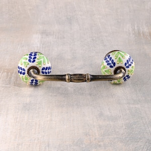 以下が含まれることがあります： 真鍮仕上げの装飾的なキャビネットプルと2つのセラミックノブ。ノブは緑、白、青で、花柄です。