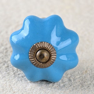 Puede incluir: Un pomo de armario de cerámica azul claro con un borde festoneado y un centro de color latón.