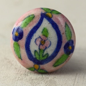 Puede incluir: Un pomo redondo de cerámica con fondo rosa y un diseño paisley azul y blanco. El paisley está rodeado de hojas verdes y flores azules.