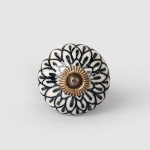 May include: White ceramic knob with a black floral design and a gold metal base.