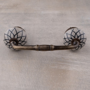 May include: A white ceramic cabinet pull with a black geometric design. The pull has a brass finish and a curved shape.