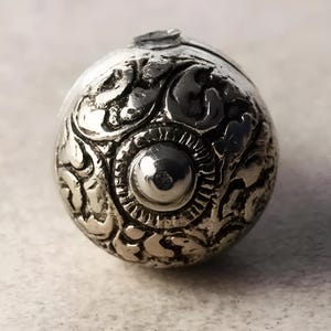 May include: A silver sphere with intricate floral designs and a raised center circle.