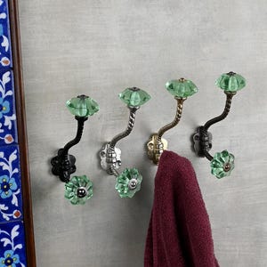 May include: Five decorative hooks with a twisted metal design and green glass knobs. A burgundy towel is hanging on one of the hooks.