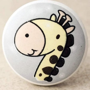 May include: A white ceramic knob with a cartoon giraffe design. The giraffe is yellow with black spots and has a light pink face.