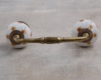 May include: White ceramic drawer pull with brown polka dots and a brass bar connecting the two knobs.