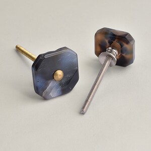 May include: Two black and white patterned cabinet knobs with gold accents and silver screws. The knobs are octagonal in shape.