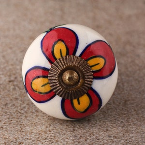 May include: White ceramic knob with a red and yellow flower design. The knob has a brass screw in the centre.