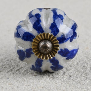 Könnte beinhalten: Ein weißer Keramik-Knopf mit einem blauen und weißen Blumenmuster und einem goldenen Metallakzent. Der Knopf ist in Form eines Kürbisses.