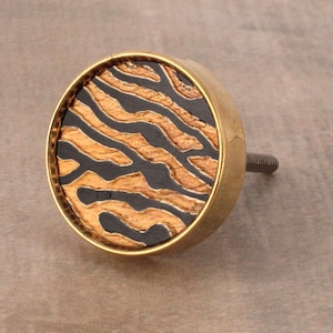 Op de afbeelding: Een ronde kastknop in goud met een zwart en gouden zebraprint.