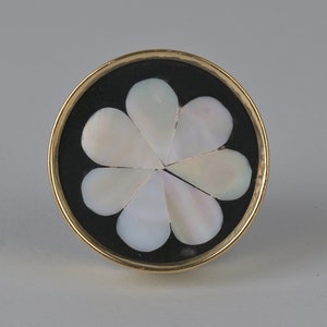 May include: A round, gold-rimmed knob with a black background and a white, mother-of-pearl flower design.