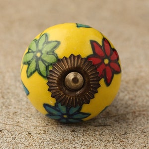 May include: Yellow ceramic knob with a floral design in shades of green, red, and blue. The knob has a brass screw in the center.