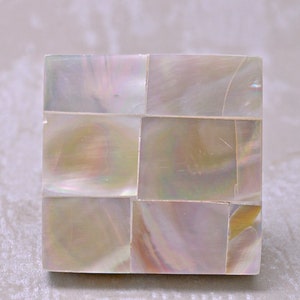 May include: A rectangular box made of iridescent mother of pearl tiles. The tiles are arranged in a grid pattern and have a subtle shimmer.