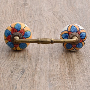 May include: A pair of ceramic drawer pulls with a floral design in shades of blue, orange, and yellow. The pulls are attached to a brass bar.