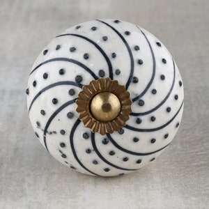 Könnte beinhalten: Weißer Keramik-Knopf mit schwarzem Spiral- und Tupfenmuster. Der Knopf hat eine goldene Metallbasis.