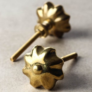 Könnte beinhalten: Zwei goldfarbene Metall-Schrankknöpfe mit einem blumenförmigen Design. Die Knöpfe haben eine Schraubbefestigung.