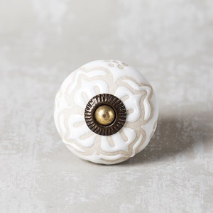 May include: White ceramic knob with a floral design and a brass accent. The knob is round and has a smooth finish.