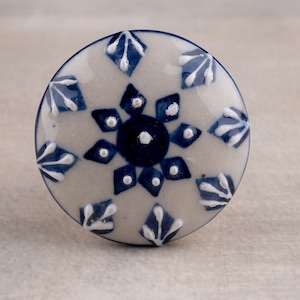 May include: A white ceramic knob with a blue and white floral design. The knob is round and has a smooth surface.