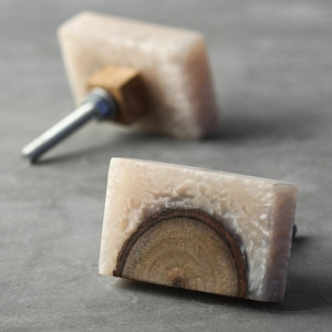 May include: Two rectangular cabinet knobs with a wood and resin design. One knob is white with a brown wood accent, and the other knob is a light brown with a wood accent.