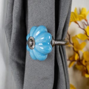 May include: A blue ceramic curtain tieback with a floral design. The tieback is attached to a silver metal rod.