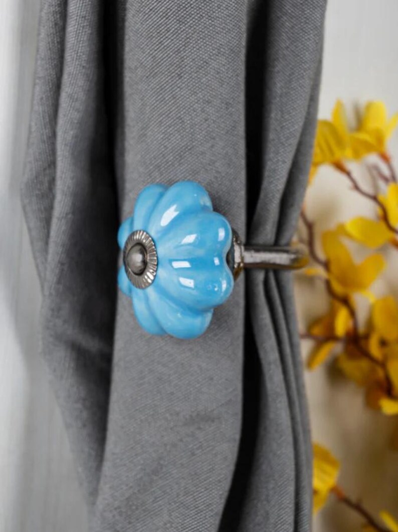 May include: A blue ceramic curtain tieback with a floral design. The tieback is attached to a silver metal rod.