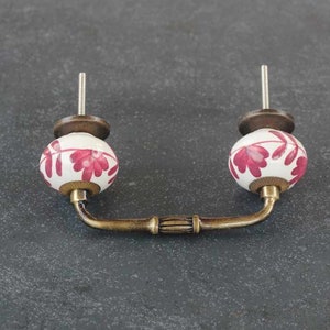 May include: A white ceramic cabinet knob with a pink floral design and a brass handle.