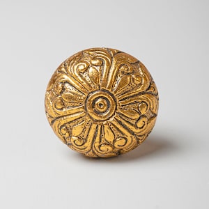 Può includere: Un pomello rotondo dorato con un intricato disegno floreale.