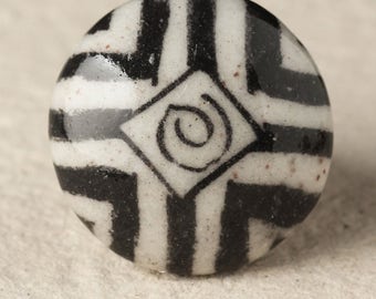 Peut inclure: Un bouton rond en céramique blanche avec un motif géométrique noir et blanc. Le motif présente une forme de diamant avec un tourbillon à l'intérieur et des rayures noires autour du bord.