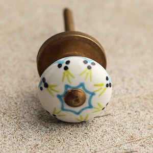 Puede incluir: Un pomo de cerámica blanca con un diseño floral azul y verde. El pomo tiene una base de latón y un tornillo.