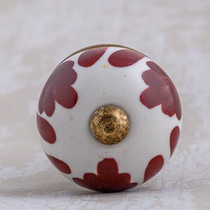 Puede incluir: Pomo de cerámica blanco con un patrón floral rojo y un centro dorado.