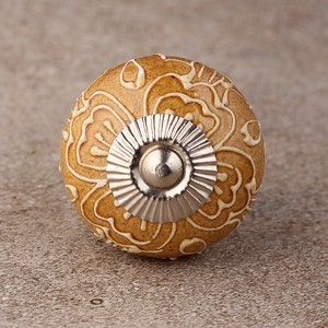 May include: A ceramic knob with a floral design in white on a brown background. The knob has a silver metal base.