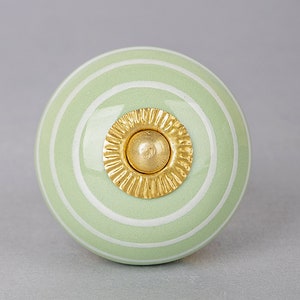 May include: A green ceramic knob with white stripes and a gold center. The knob is round and has a smooth surface.