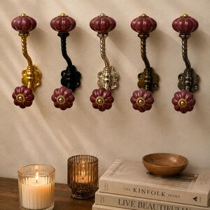 May include: Five wall-mounted hooks featuring dark maroon, pumpkin-shaped ceramic knobs at the top and bottom. The metal stems vary in finish, including gold, black, silver, and antique bronze, each with a twisted design and a decorative base plate.