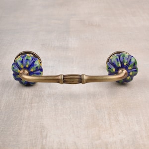 Peut inclure: Une poignée de tiroir en céramique bleue et jaune avec une arche en laiton. La céramique est peinte à la main avec un motif floral.