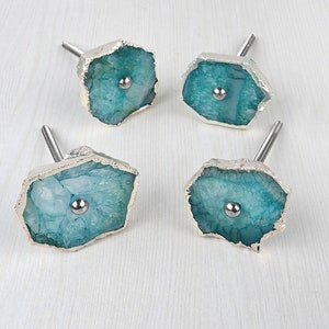 Puede incluir: Conjunto de cuatro tiradores de cajón de ágata azul verdoso con detalles en metal plateado. Cada tirador presenta un patrón de ágata natural único y una perilla de metal plateado.